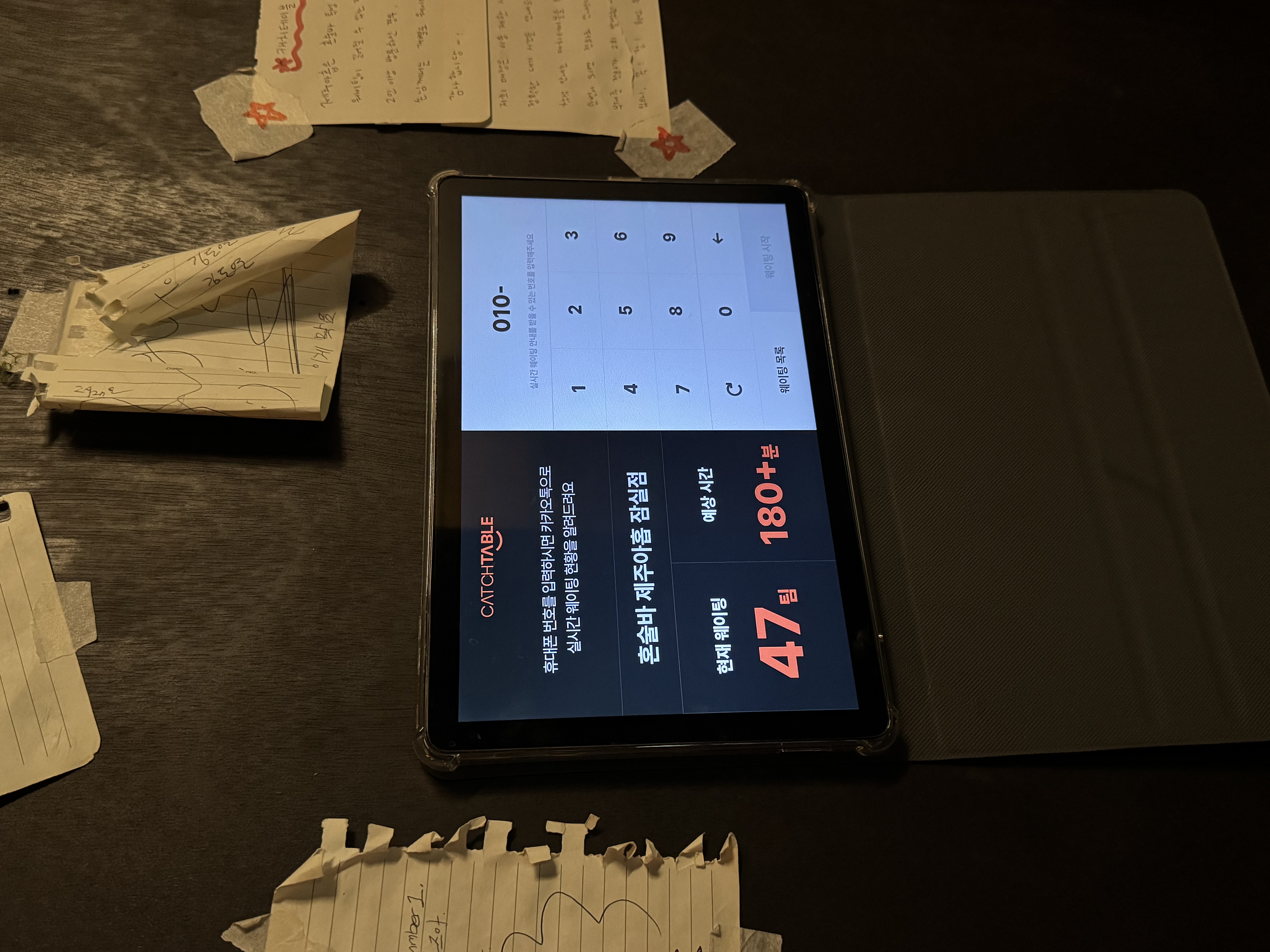 테이블 위에 놓인 태블릿에 '캐치테이블' 웨이팅 접수 화면이 떠 있으며 현재 대기 47팀, 예상 시간 180분 이상이 표시된 매장 안내판 사진이다.