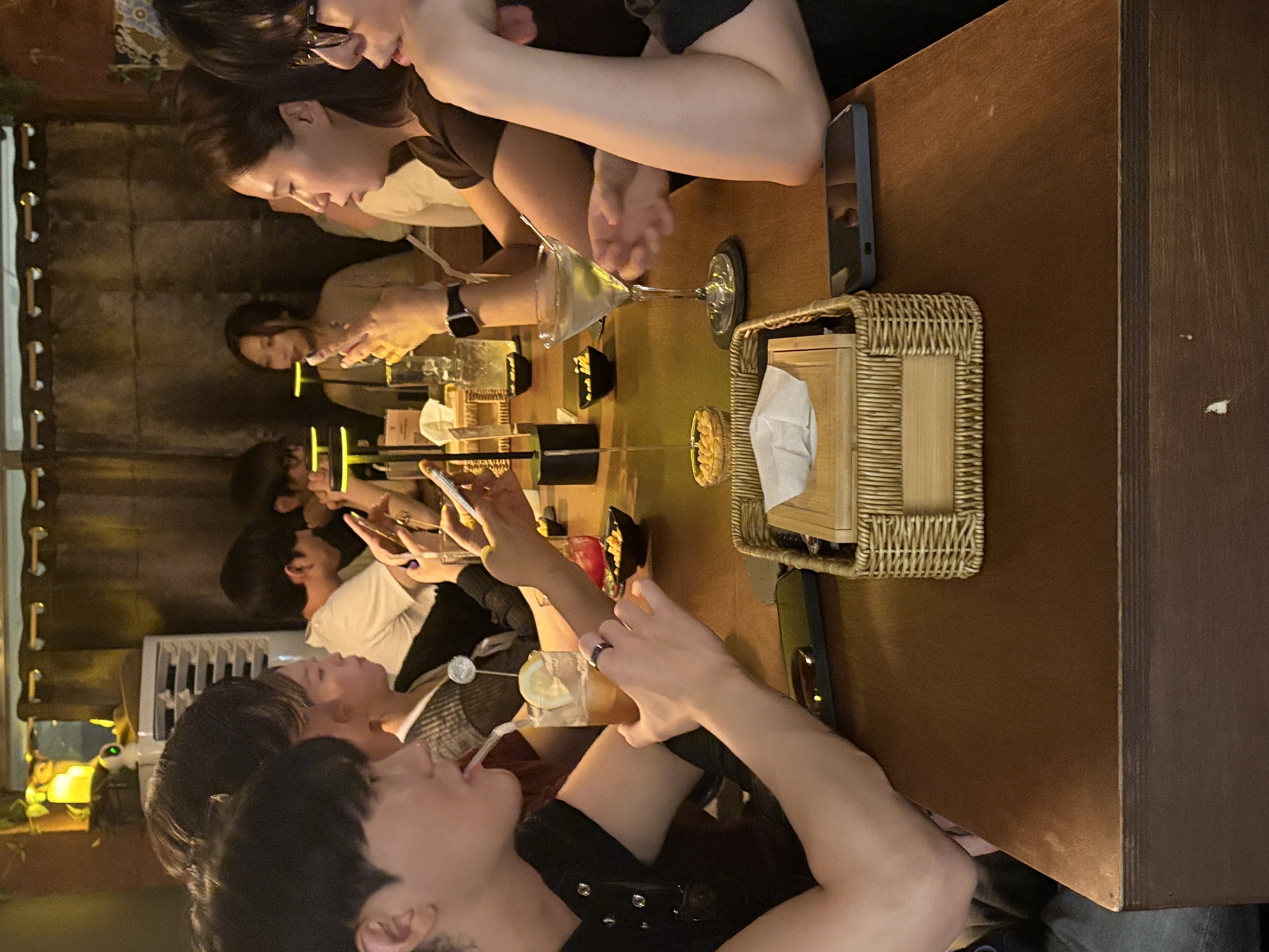 테이블에 둘러앉은 손님들이 마티니 잔과 하이볼 잔을 앞에 두고 즐겁게 대화하는 단체 모임 사진이다.
