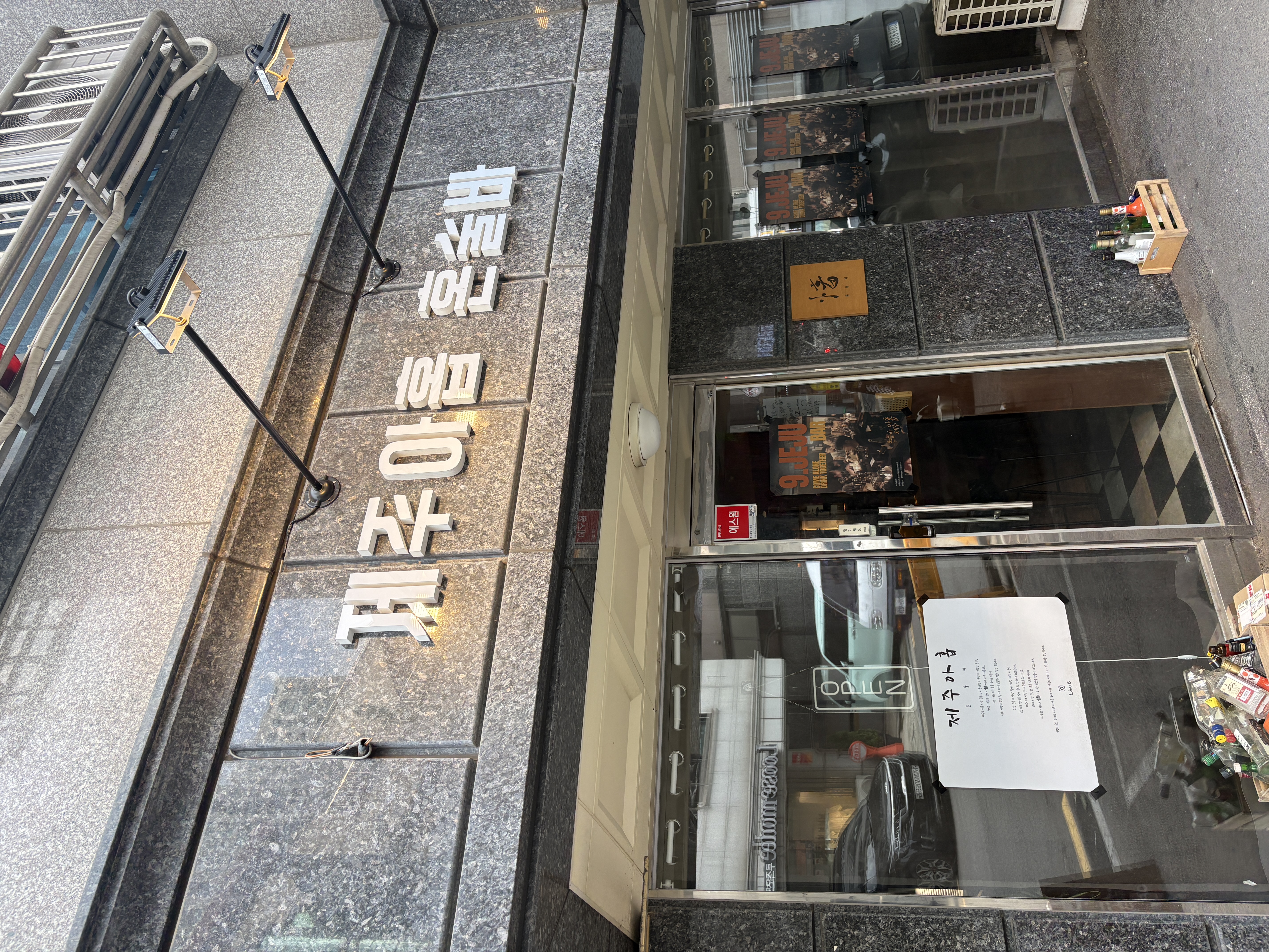 외관 사진: 매장 정면 클로즈업으로 '제주아홉' 간판 글자와 유리문에 붙은 '9.JEJU' 포스터, 입구 진열대가 보이는 모습