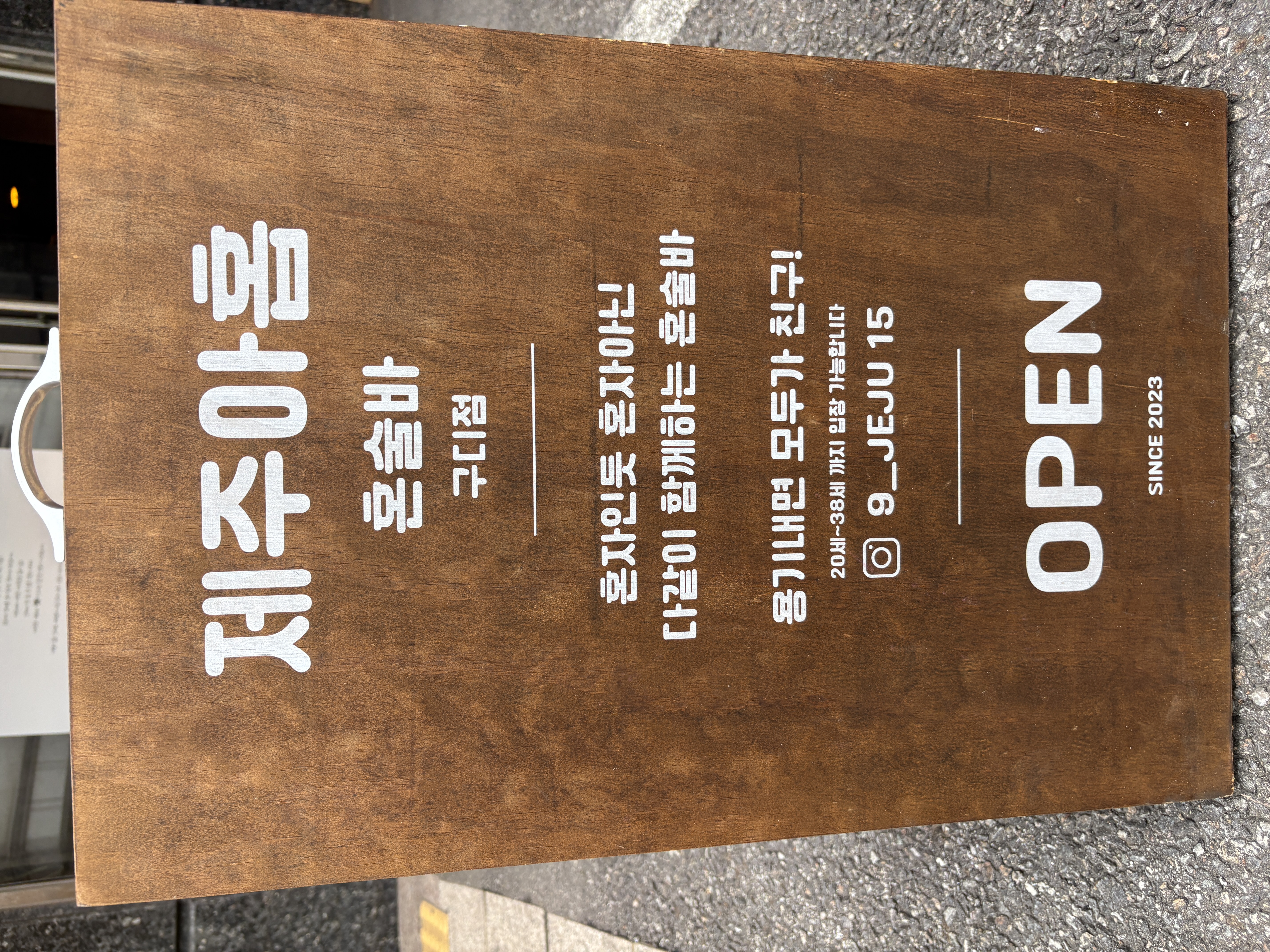 안내판 사진: 목재 입간판에 적힌 '제주아홉 혼술바 구디점' 문구와 '혼자인듯 혼자아닌 다같이 함께하는 혼술바', '용기내면 친구! 20세~38세 가능합니다', 인스타그램 계정, 'OPEN SINCE 2023' 안내 문구