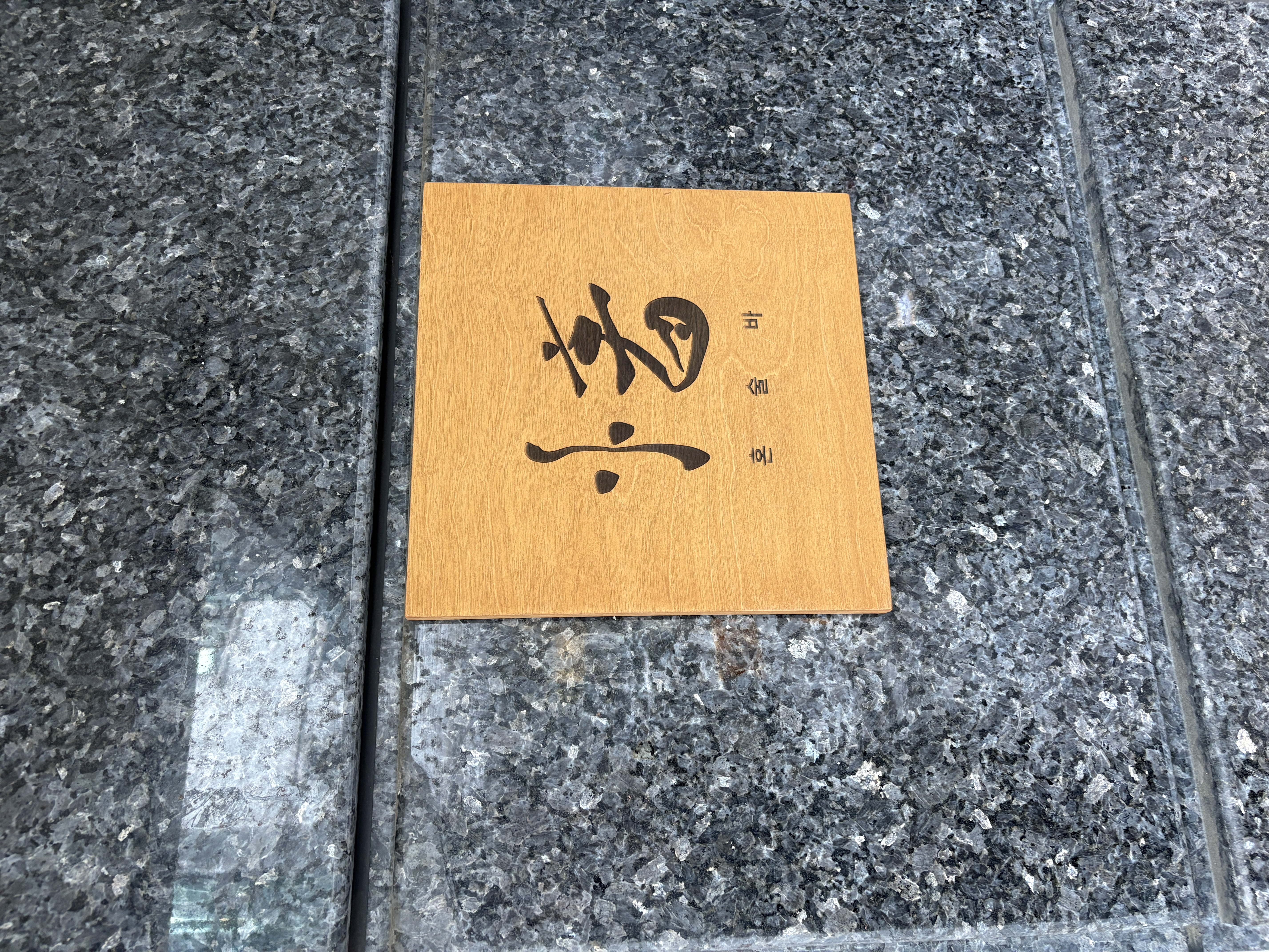 간판 클로즈업 사진: 화강암 외벽에 부착된 원목 로고 간판으로 캘리그래피 스타일의 상호명이 새겨져 있는 모습