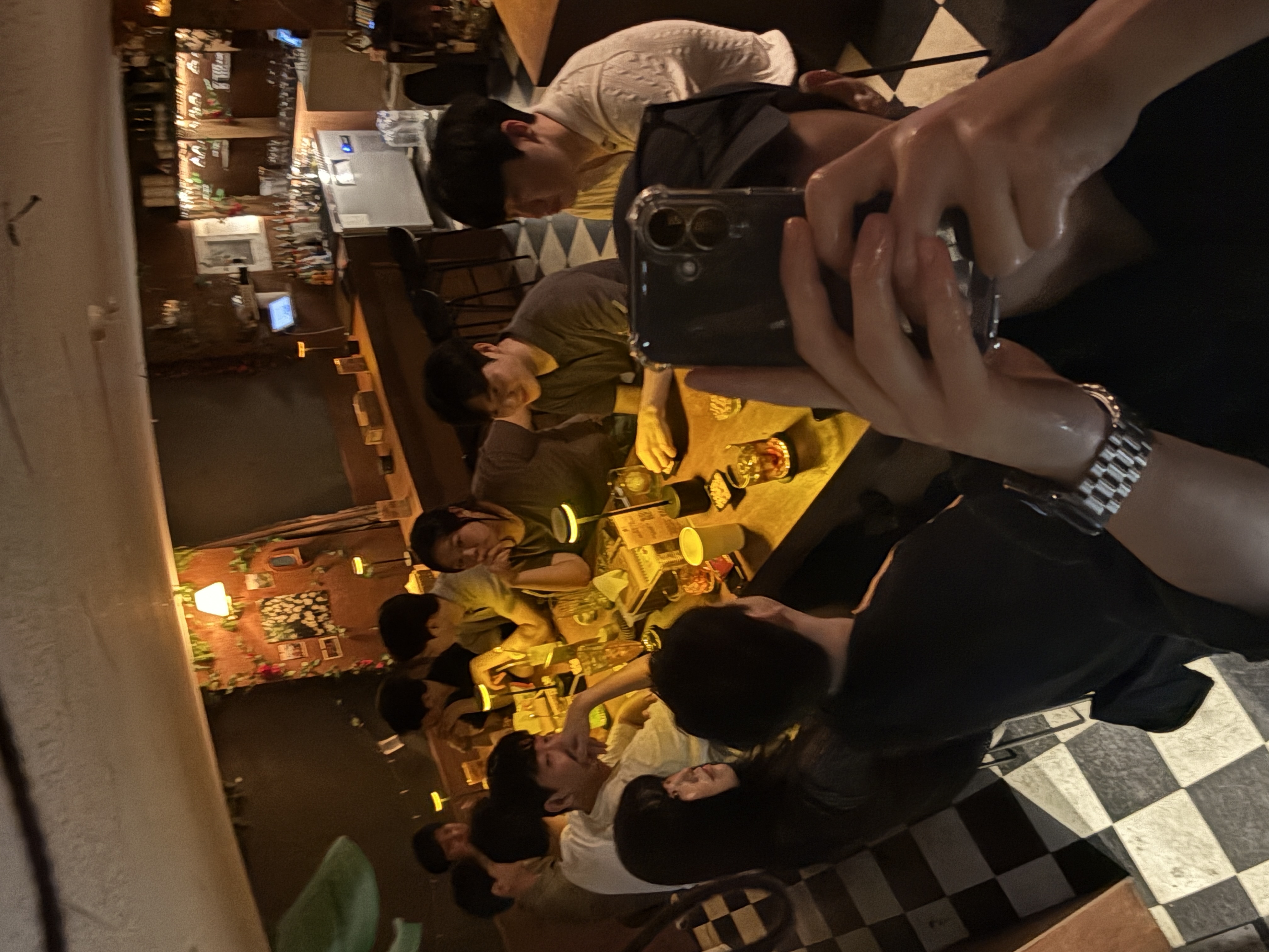 저녁 시간대 매장 테이블에 둘러앉은 손님들이 음료와 안주를 앞에 두고 함께 셀카를 찍는 화기애애한 모임 장면.